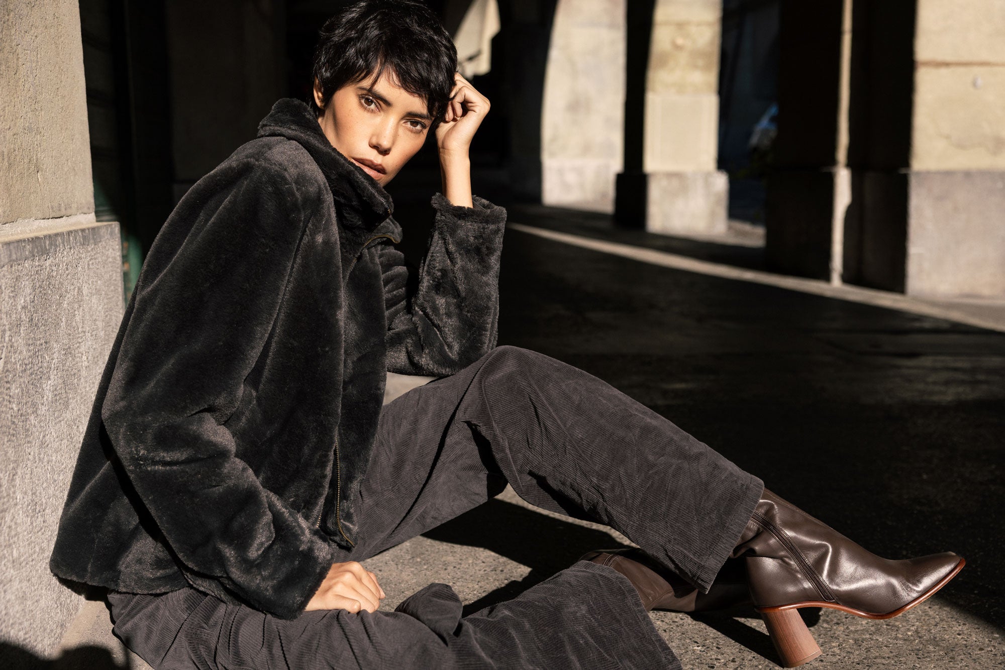 Une femme est assise par terre, adossée à un mur, et pose pour la caméra.