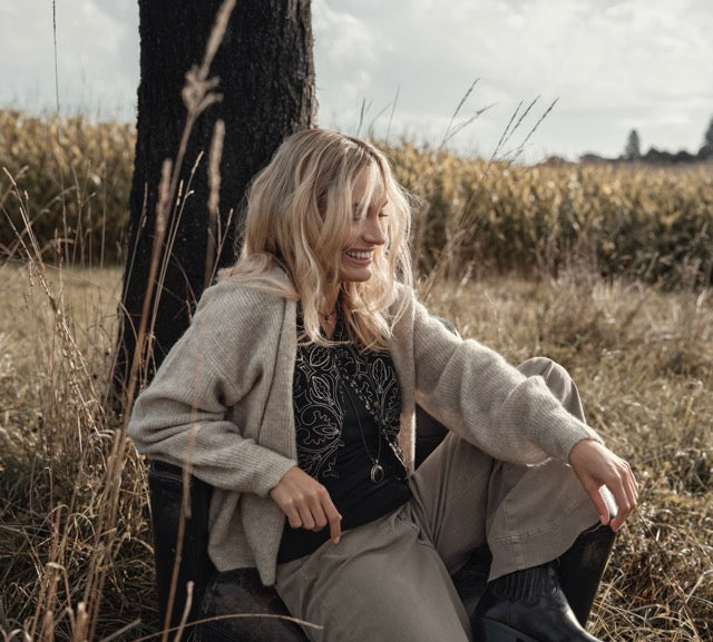 Eine Frau sitzt auf einem Ledersessel und lächelt. Sie trägt ein Oufit von Bijou les Boutiques.