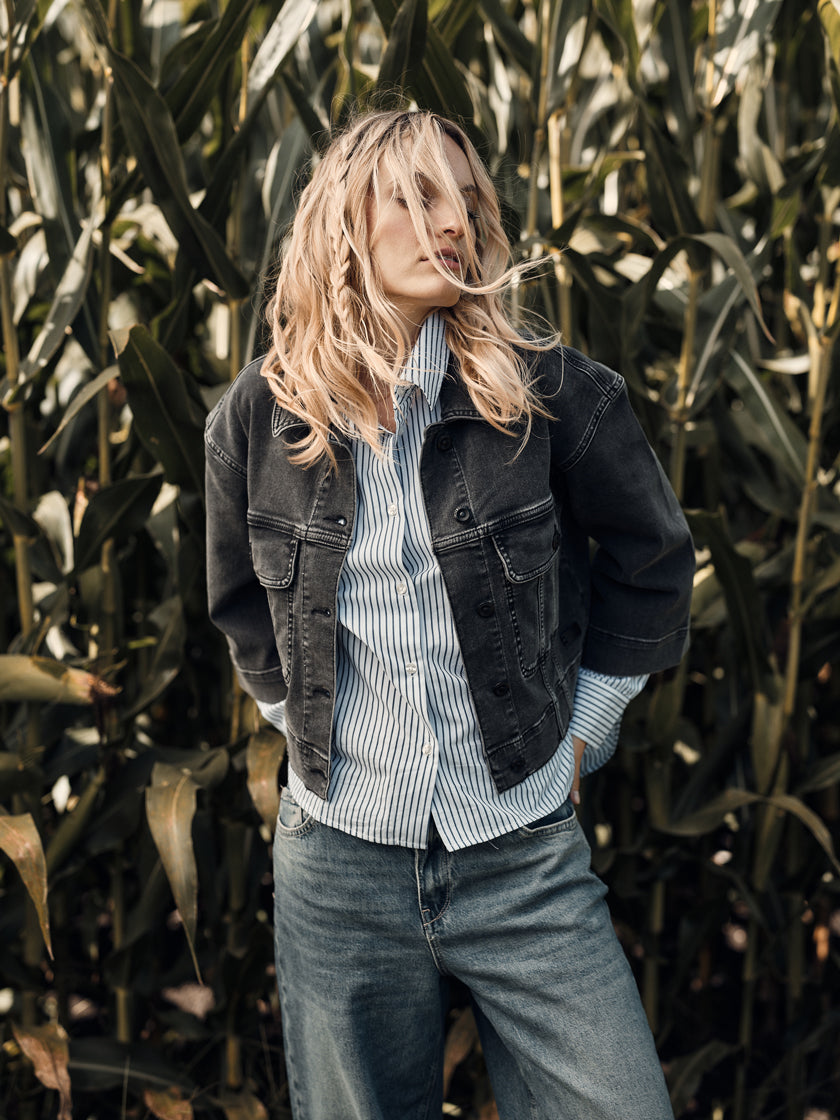 Eine blonde Frau posiert vor einem Maisfeld in ihrem Denim-Look. 